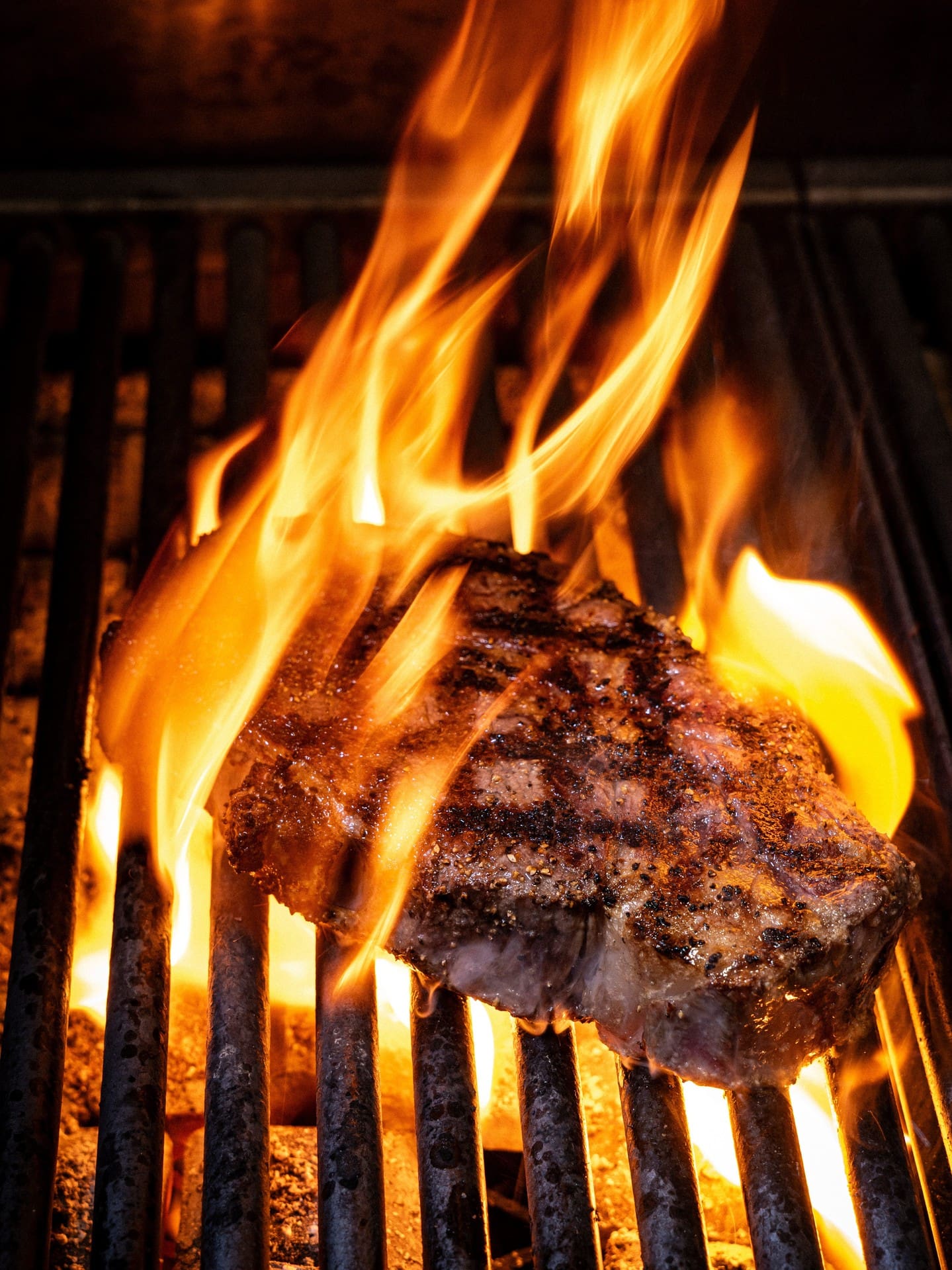 A steak on a barbecue with large flames rising around it.