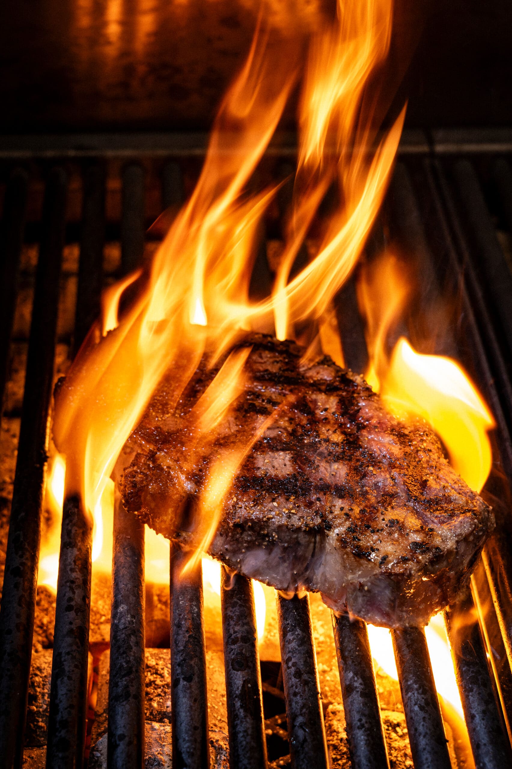 A steak with grill marks is being cooked over open flames on a barbecue.