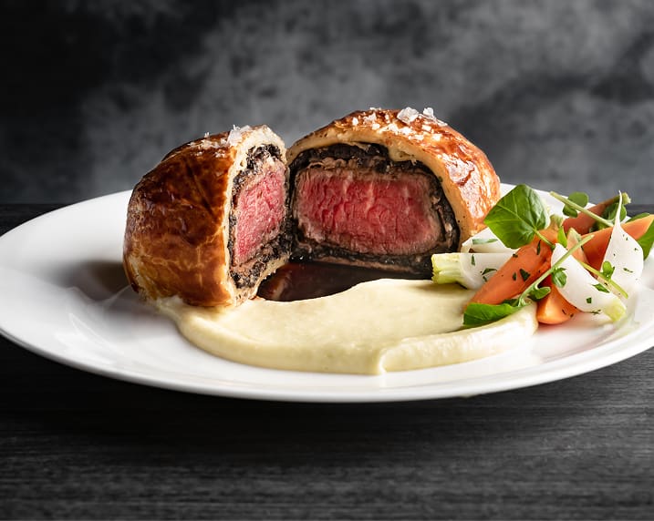 Beef Wellington with mashed potatoes and mixed vegetables on a white plate.