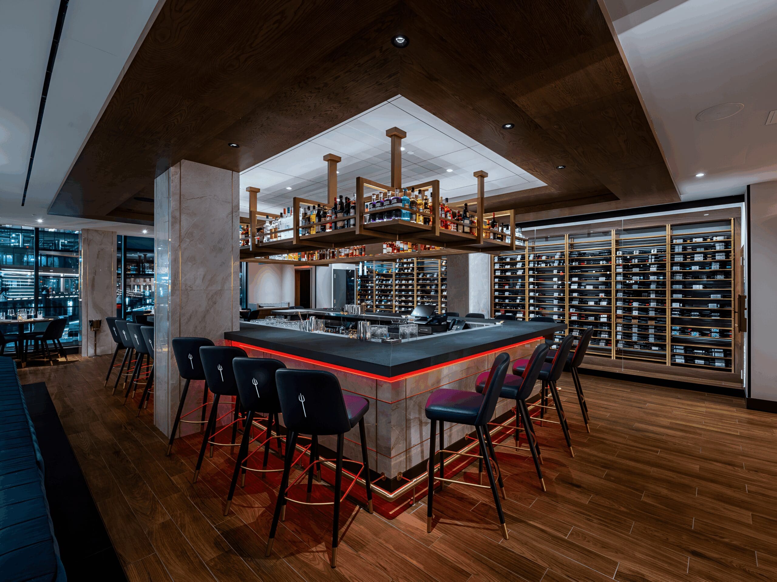 A modern wine bar with high stools, wooden floors, and shelves of wine bottles on the walls.