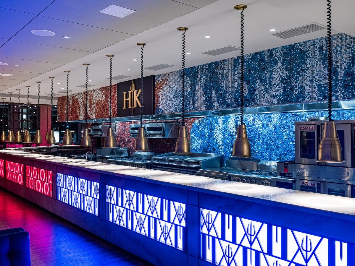 Modern, stylish restaurant kitchen with blue and red mosaic walls, lit counters, and hanging lights.